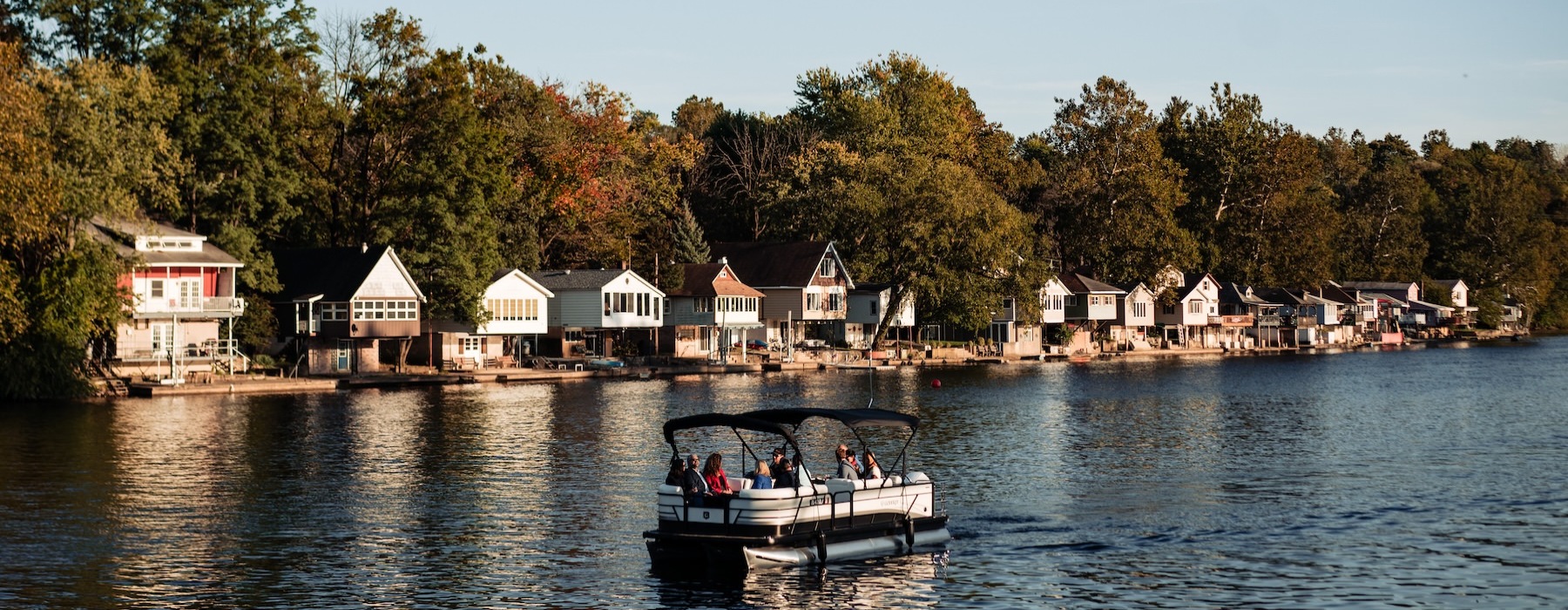 a river with people on a boat and houses with trees